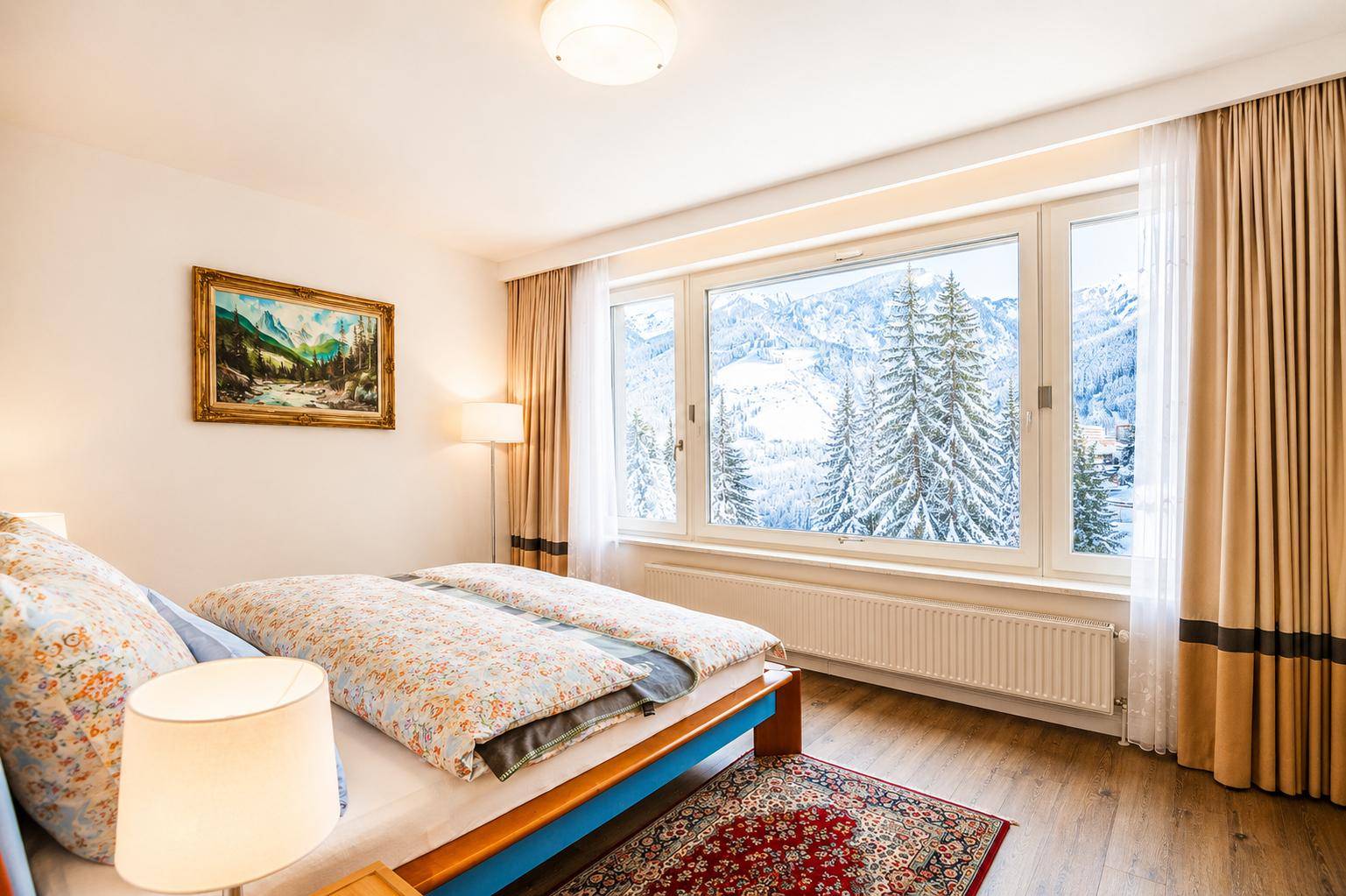 Gemütliches Schlafzimmer mit Doppelbett, Holzboden und weitem Blick auf die verschneiten Berge.