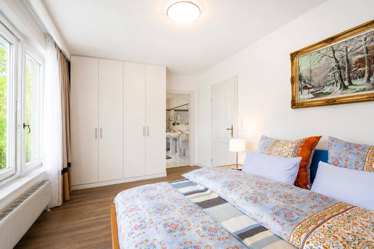 Helles Schlafzimmer mit Einbauschränken, Holzboden und Zugang zu einem angrenzenden Raum.