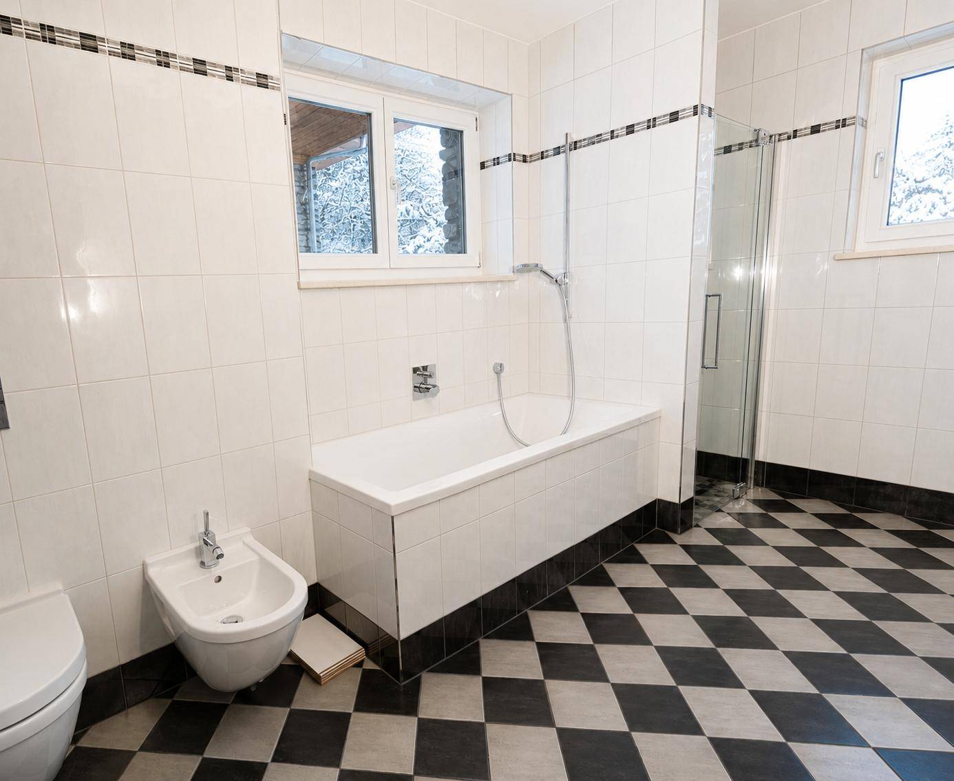 Geräumiges Badezimmer mit schwarz-weiß karierten Fliesen, Badewanne, Duschkabine und Bidet.