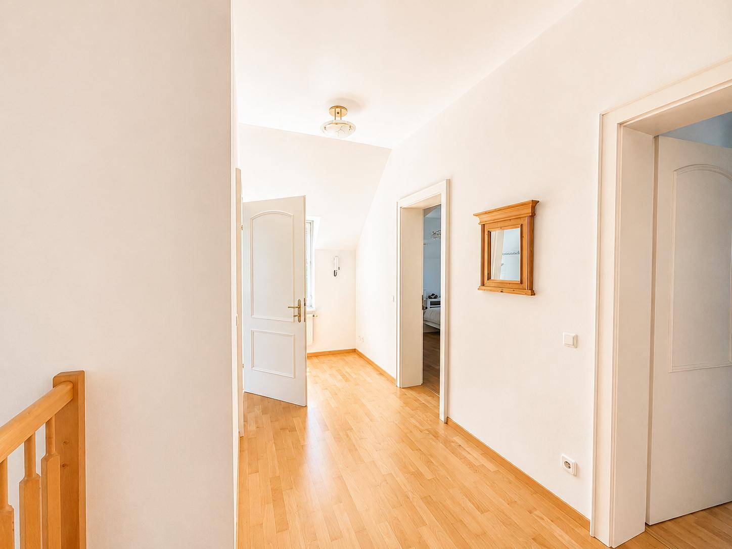 Heller Flur mit Holzfußboden und weißen Türen, der zu weiteren Räumen führt.