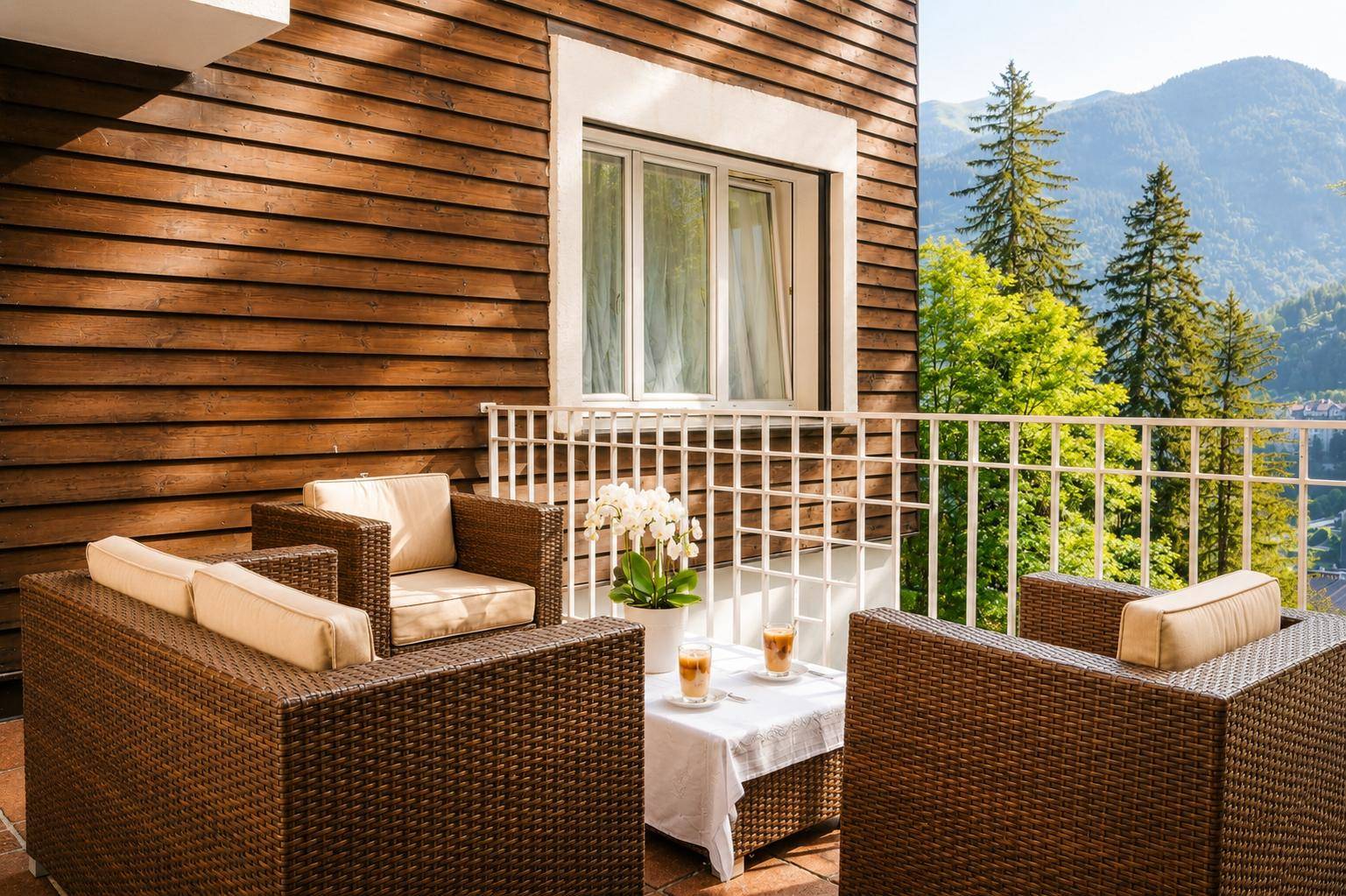 Balkon mit Rattanmöbeln und Blick auf die grüne Berglandschaft unter blauem Himmel.