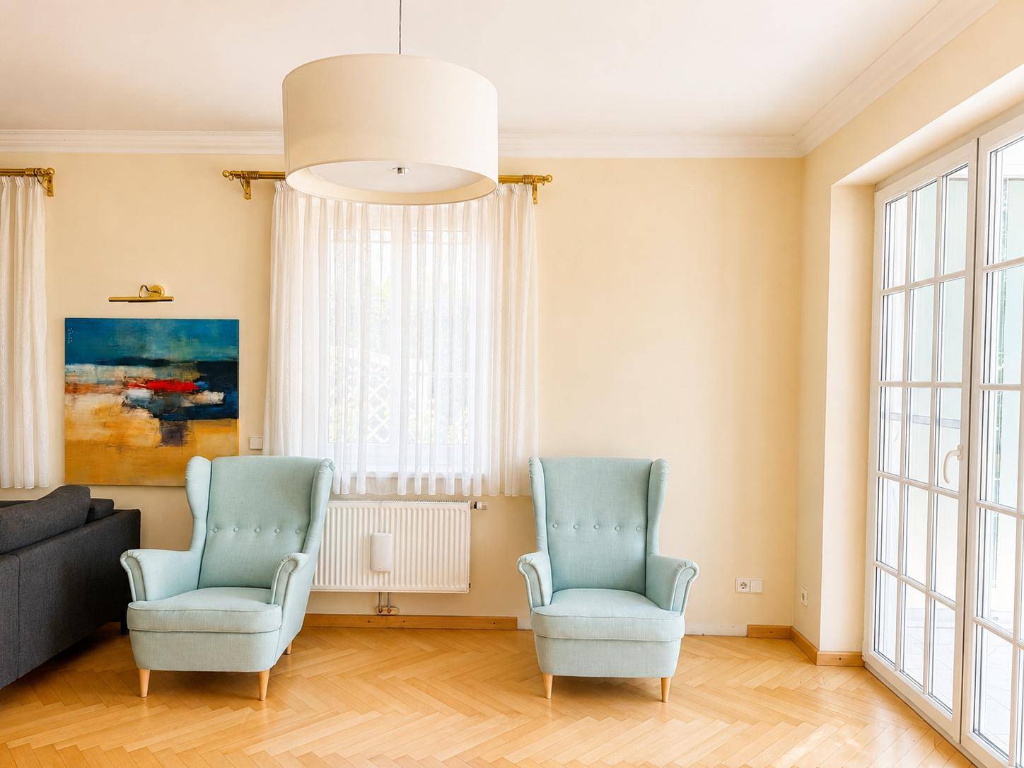 Helles Wohnzimmer mit Fischgrätparkett, großen Fenstern und Blick in den Garten.