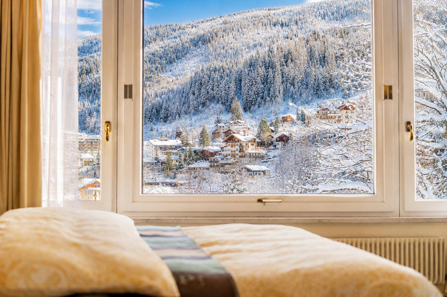 Schlafzimmer mit gemütlichem Bett und weitem Blick auf die verschneite Berglandschaft.