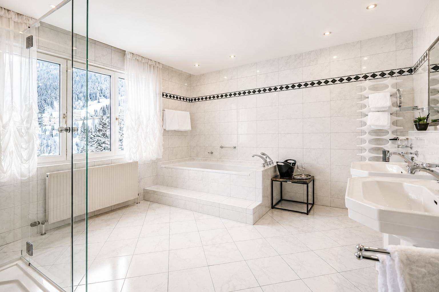 Helles Badezimmer mit großer Badewanne, Doppelwaschbecken und Blick auf die verschneite Berglandschaft.