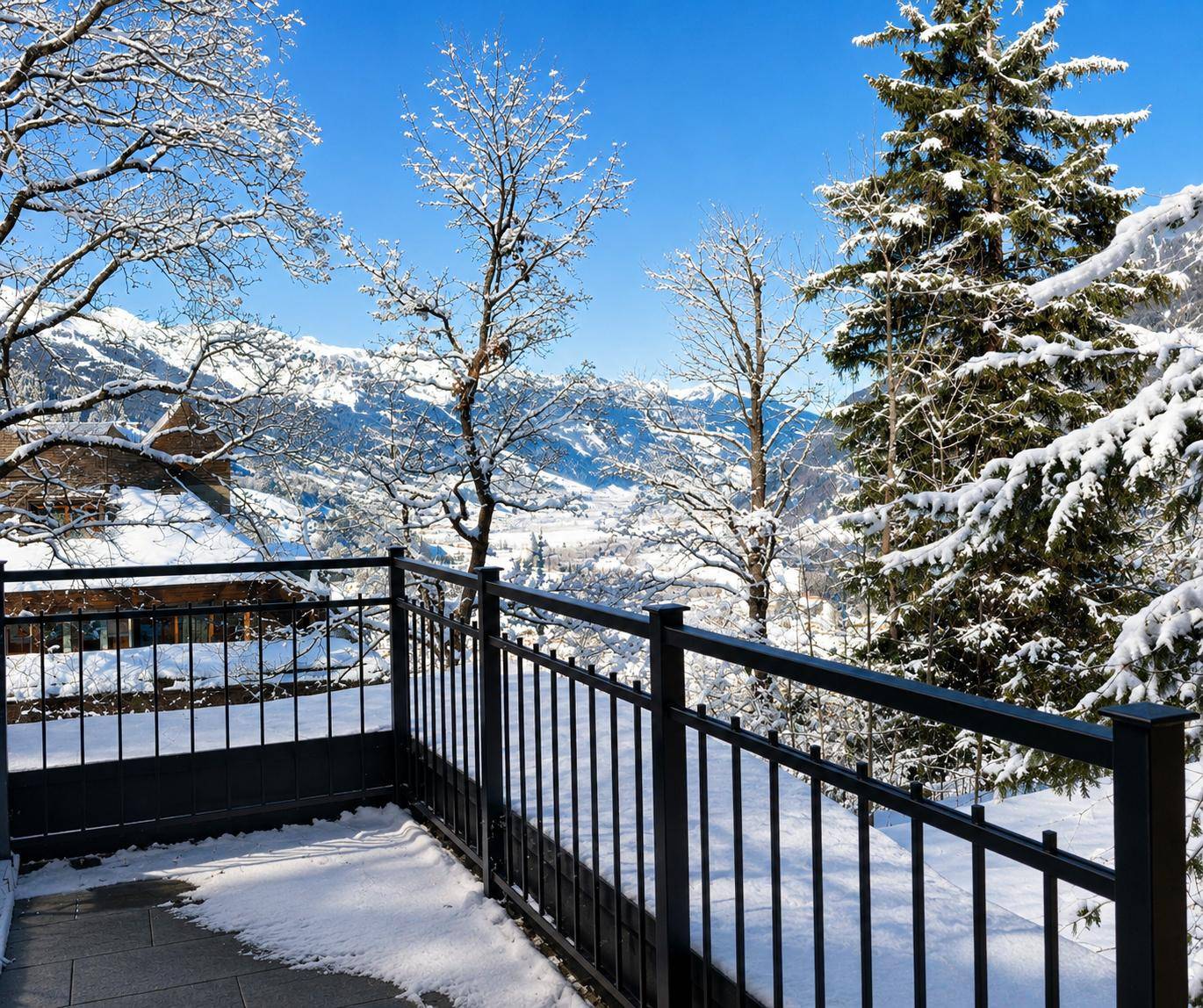 Balkon mit schwarzem Geländer und atemberaubendem Panoramablick auf die verschneiten Berge und Wälder.
