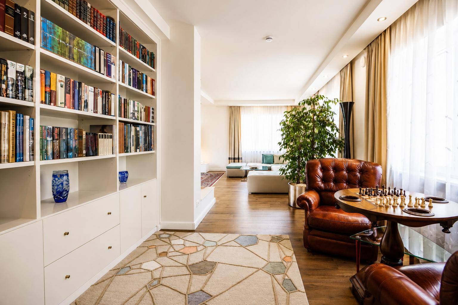Großzügiges Wohnzimmer mit Bücherregal, Ledersessel und Blick auf den Garten.