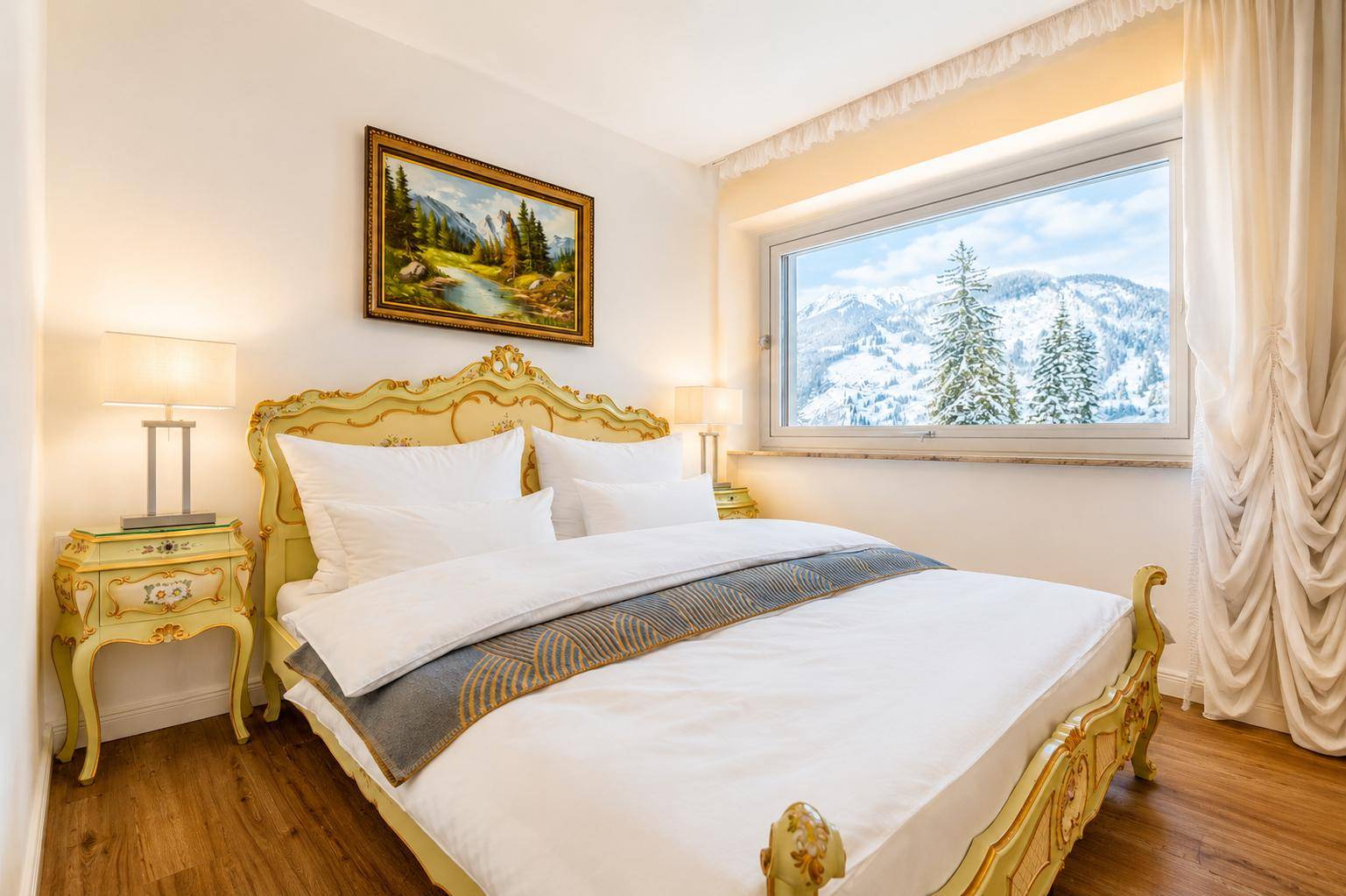 Helles Schlafzimmer mit klassischem Bett, Holzboden und weitem Blick auf die verschneiten Berge.