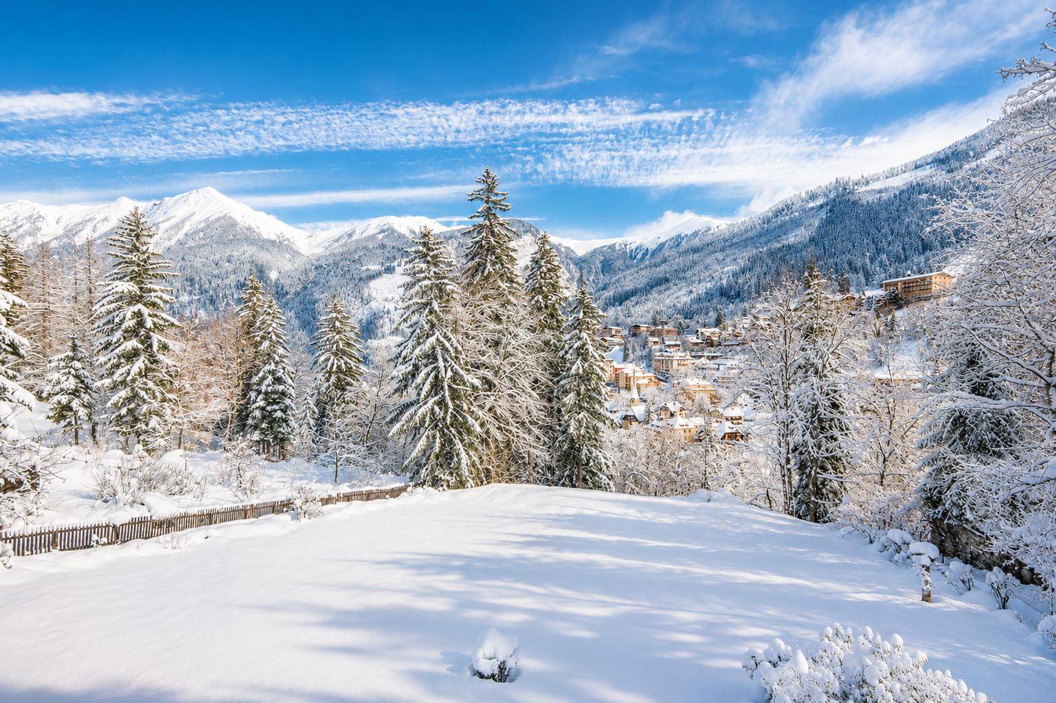 Malerische Winterlandschaft mit verschneiten Bergen, Tannenbäumen und einem Dorf im Tal.