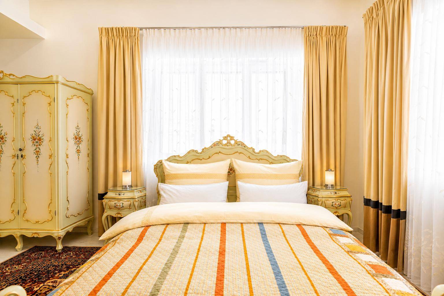 Klassisches Schlafzimmer mit einem großen Bett, verzierten Möbeln und hellen Vorhängen.