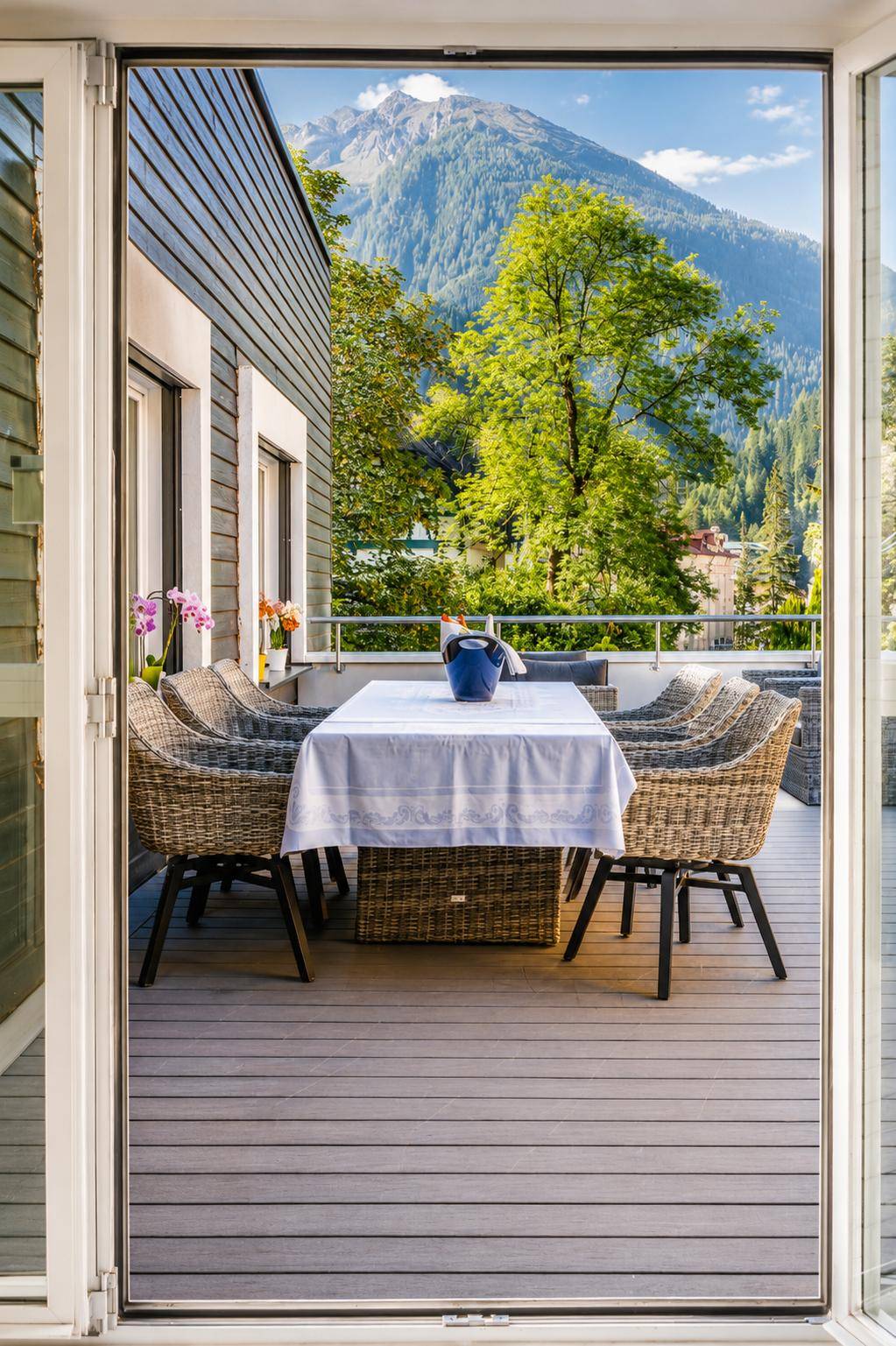 Geräumige Terrasse mit Esstisch und Korbstühlen, umgeben von grünen Bergen.