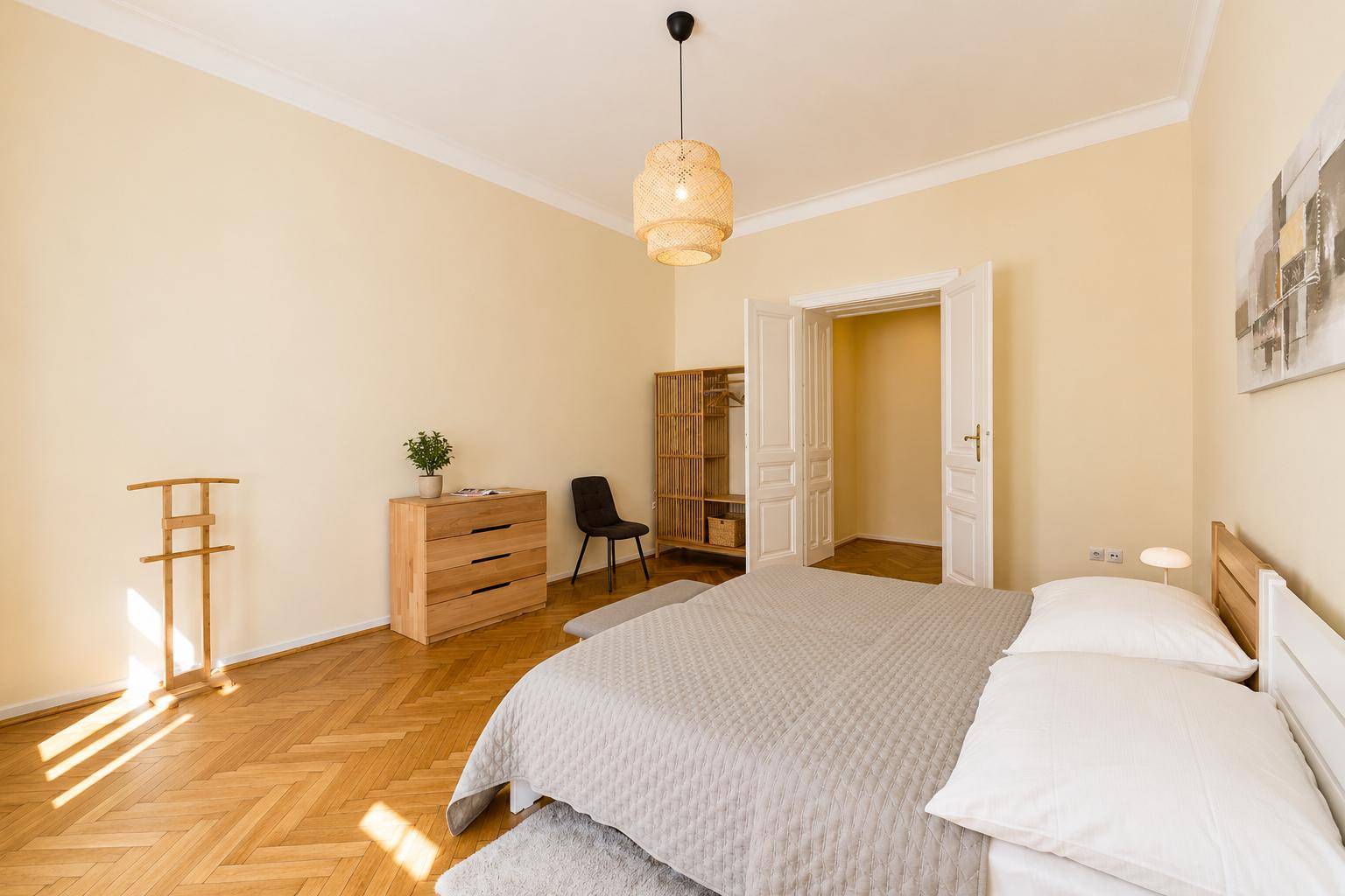 Schlafzimmer mit Doppelbett, Holzkommode und offenem Kleiderschrank, viel Tageslicht.