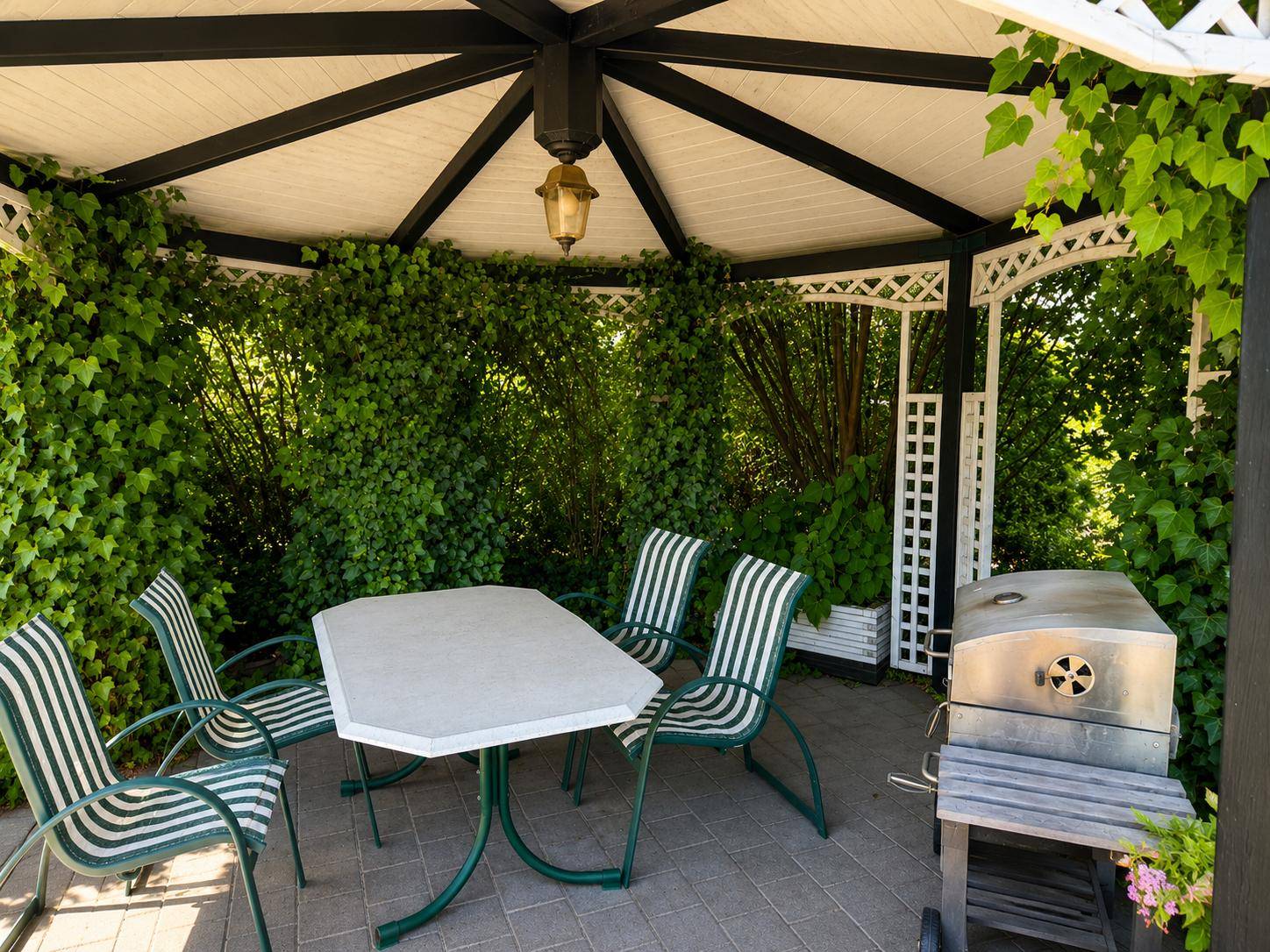Detailansicht des Gartenpavillons mit Esstisch, Stühlen und Grill für gesellige Runden.