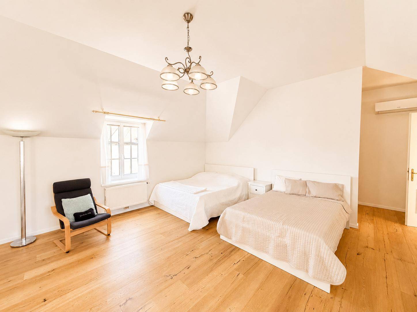 Helles Schlafzimmer im Dachgeschoss mit zwei Betten, Holzboden und Fenster.