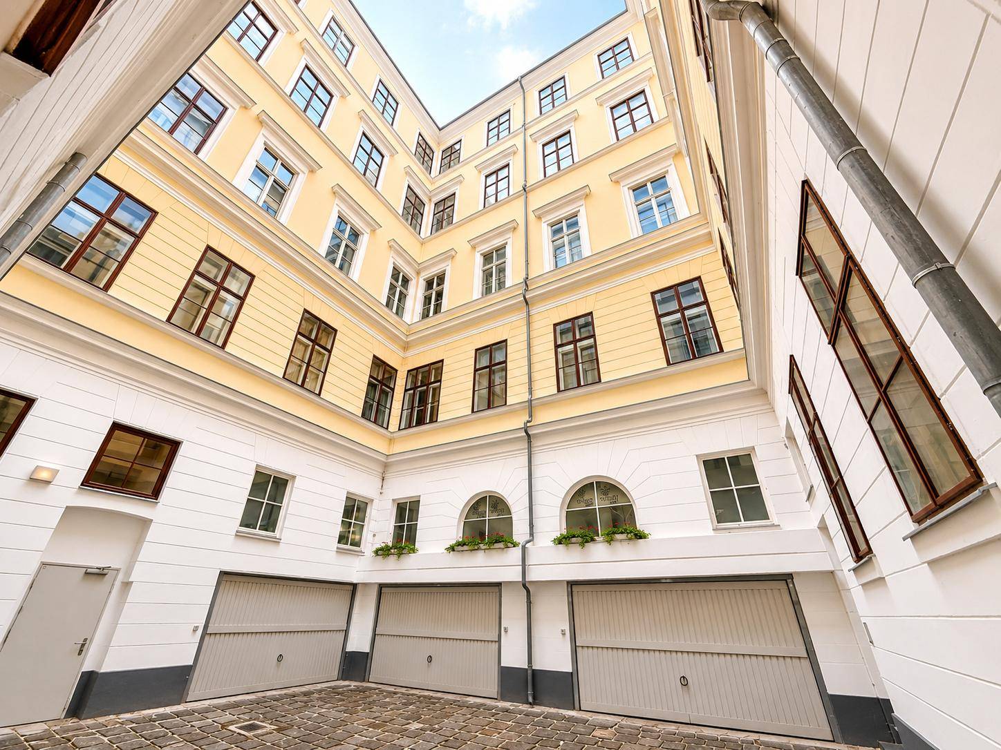 Blick in einen hellen Innenhof eines historischen Gebäudes mit Garagentoren und vielen Fenstern.