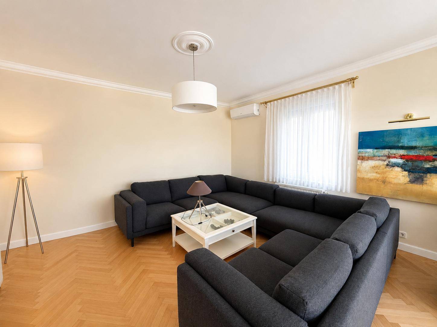 Gemütliches Wohnzimmer mit großem Ecksofa, Fischgrätparkett und moderner Kunst an der Wand.