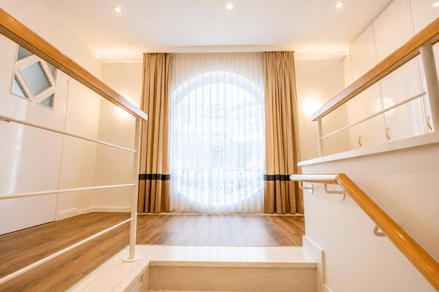 Heller Treppenabsatz mit großem Rundfenster, Holzgeländer und Einbauschränken.