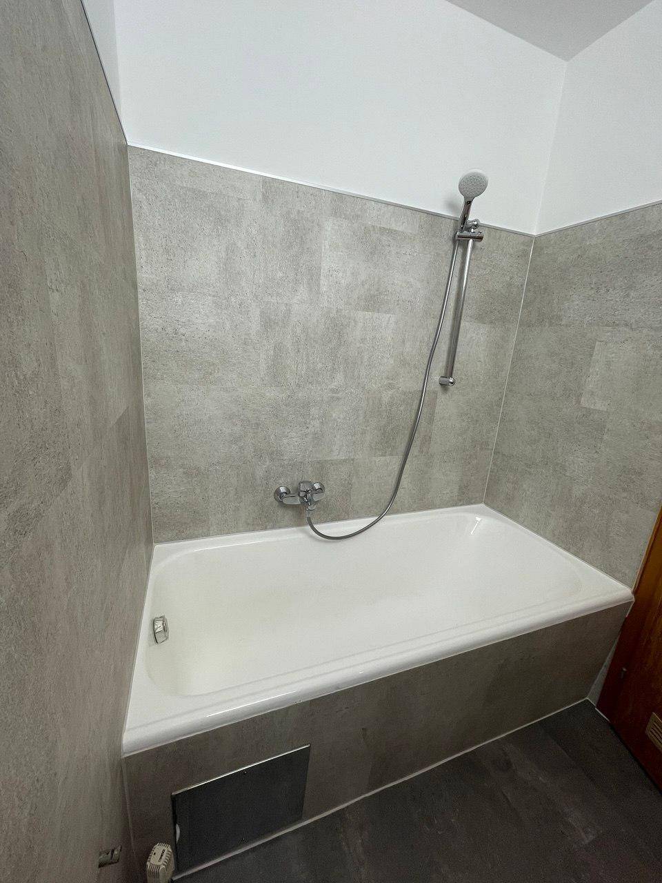 Modernes Badezimmer mit Badewanne und Duschfunktion, ausgestattet mit grauen Fliesen an Wänden und Boden.