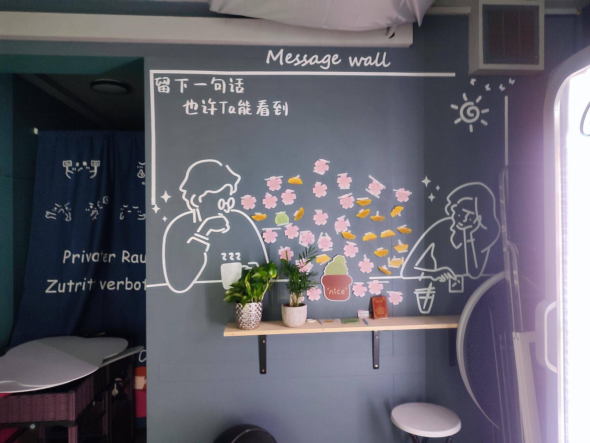 Kreativ gestaltete Wand mit handgezeichneten Figuren und einer Nachrichtenwand in einem gemütlichen Sitzbereich.