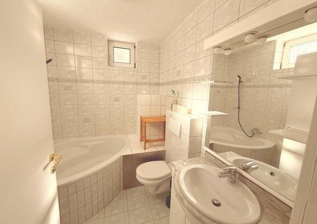 Helles Badezimmer mit Eckbadewanne, WC, Waschbecken und gefliesten Wänden.