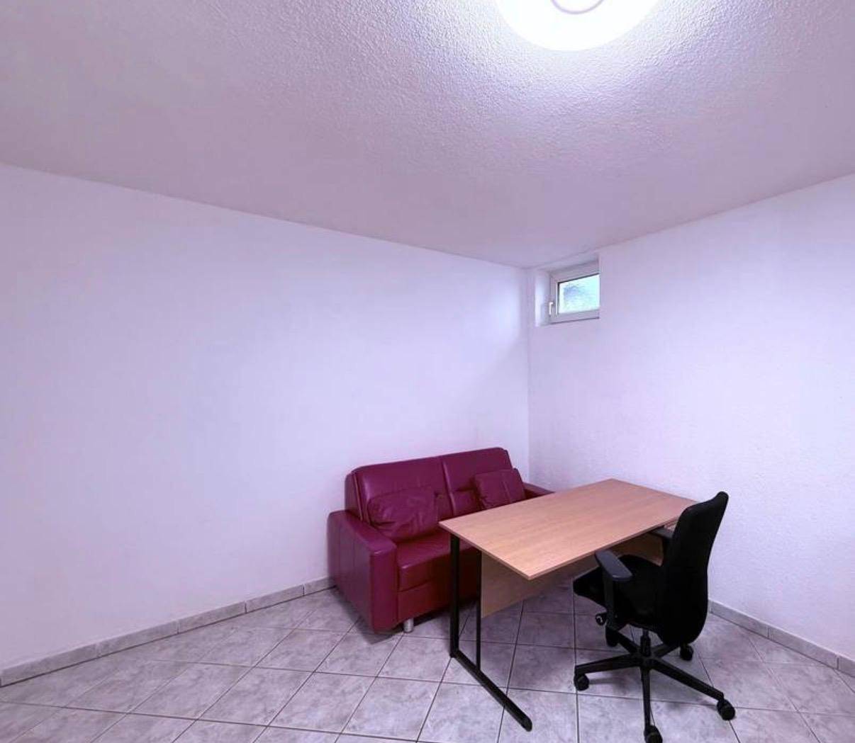 Heller Wohnraum mit rotem Sofa, Schreibtisch und kleinem Fenster.