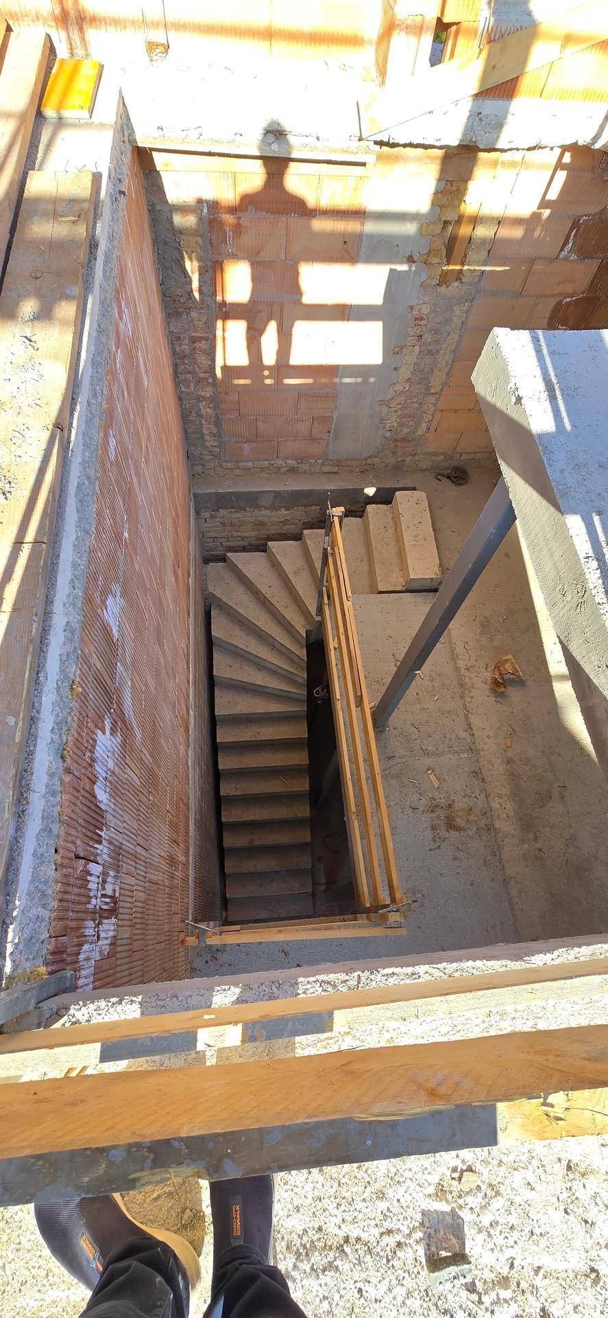 Blick von oben auf eine im Bau befindliche Betontreppe mit Ziegelwänden und Gerüst im Treppenhaus.