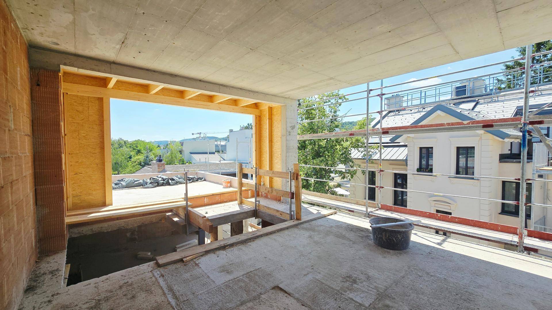Unfertiger Innenraum im Rohbau mit Blick nach draußen und Betonboden.