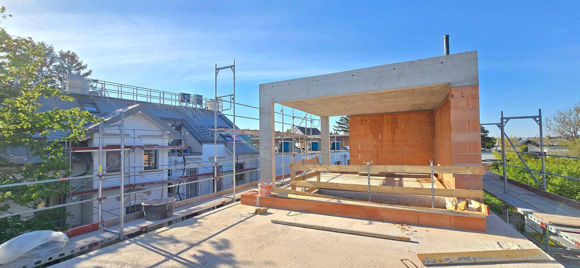 Dachterrasse im Rohbau mit Gerüst und weitem Blick über die Nachbarschaft und Bäume.