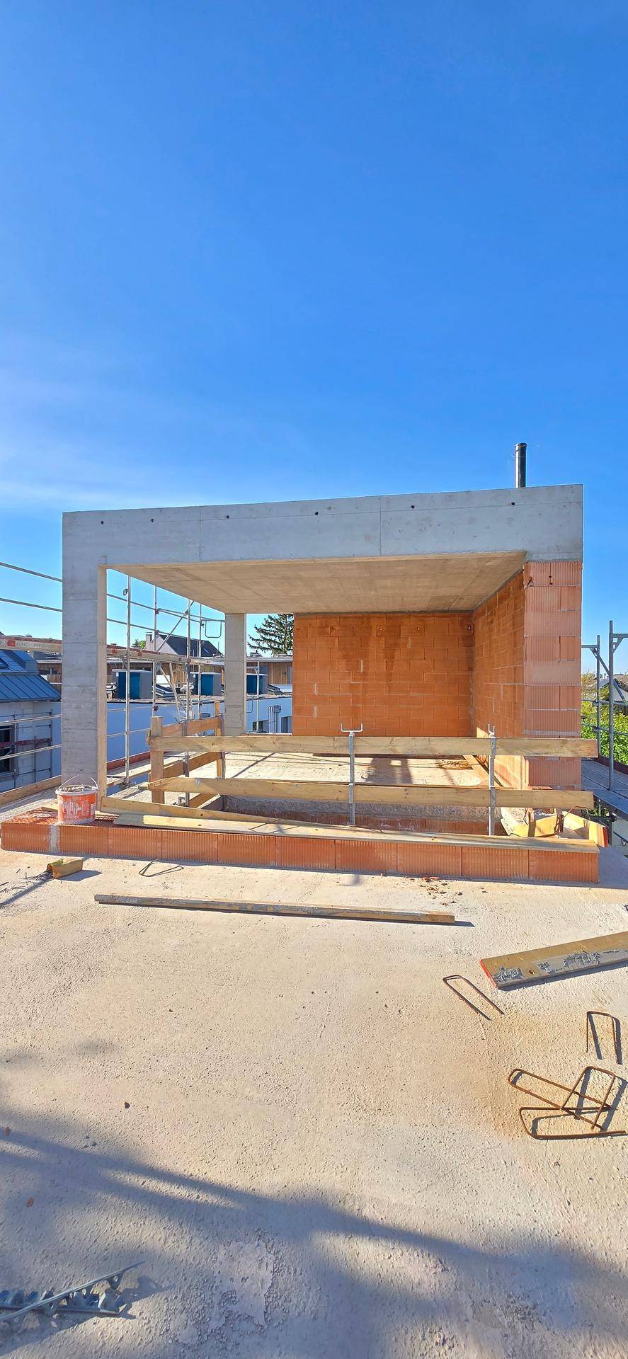 Unfertige Dachterrasse im Rohbau mit Blick auf den blauen Himmel und die Umgebung.