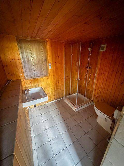 Badezimmer mit Holzverkleidung, Duschkabine, Waschbecken und WC, ausgestattet mit grauen Fliesen.