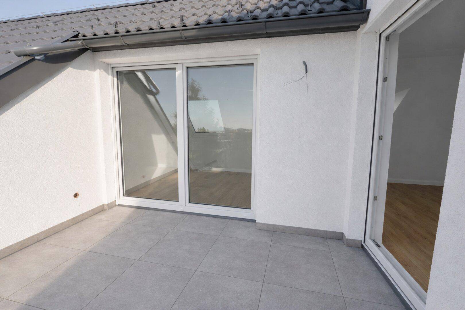 Kleine Terrasse mit Fliesenboden und Schiebetürzugang zu einem hellen Innenraum.
