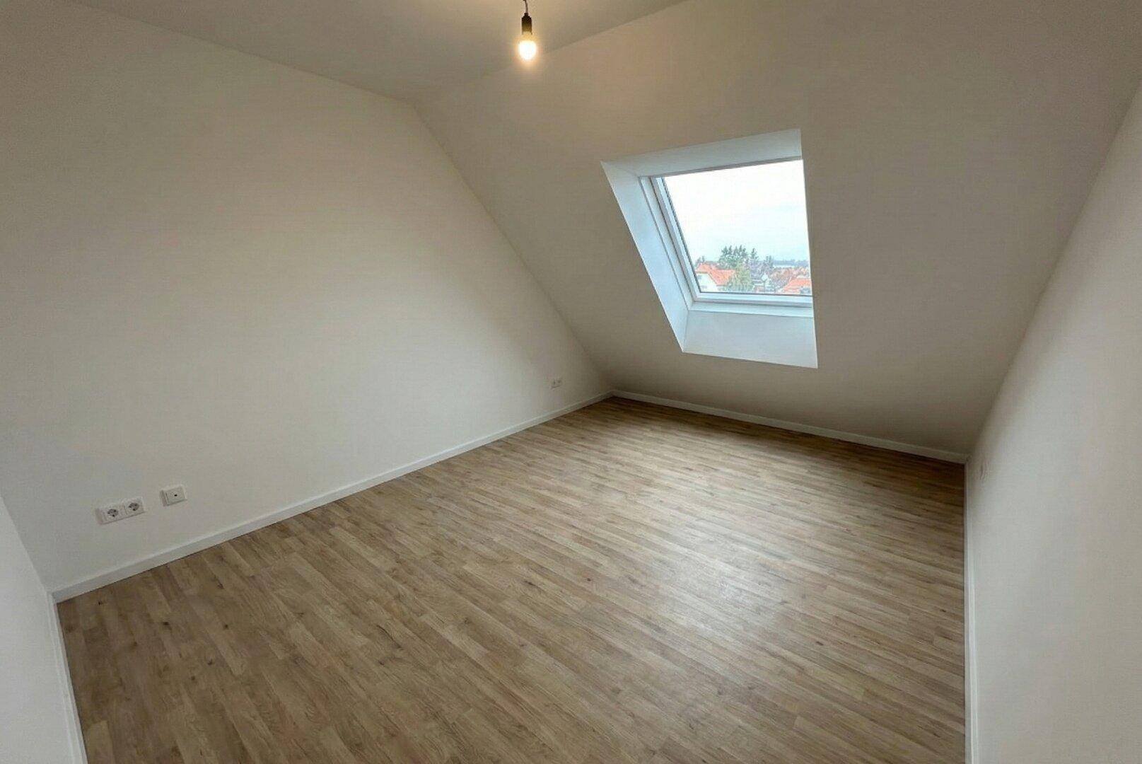 Unmöblierter Raum im Dachgeschoss mit einem großen Dachfenster und hellem Laminatboden.