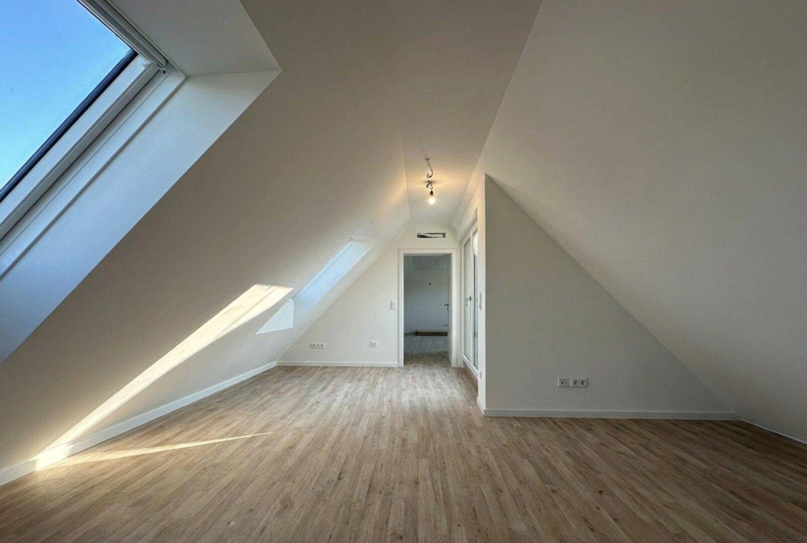 Heller Raum im Dachgeschoss mit schrägen Wänden, Dachfenstern und Laminatboden.