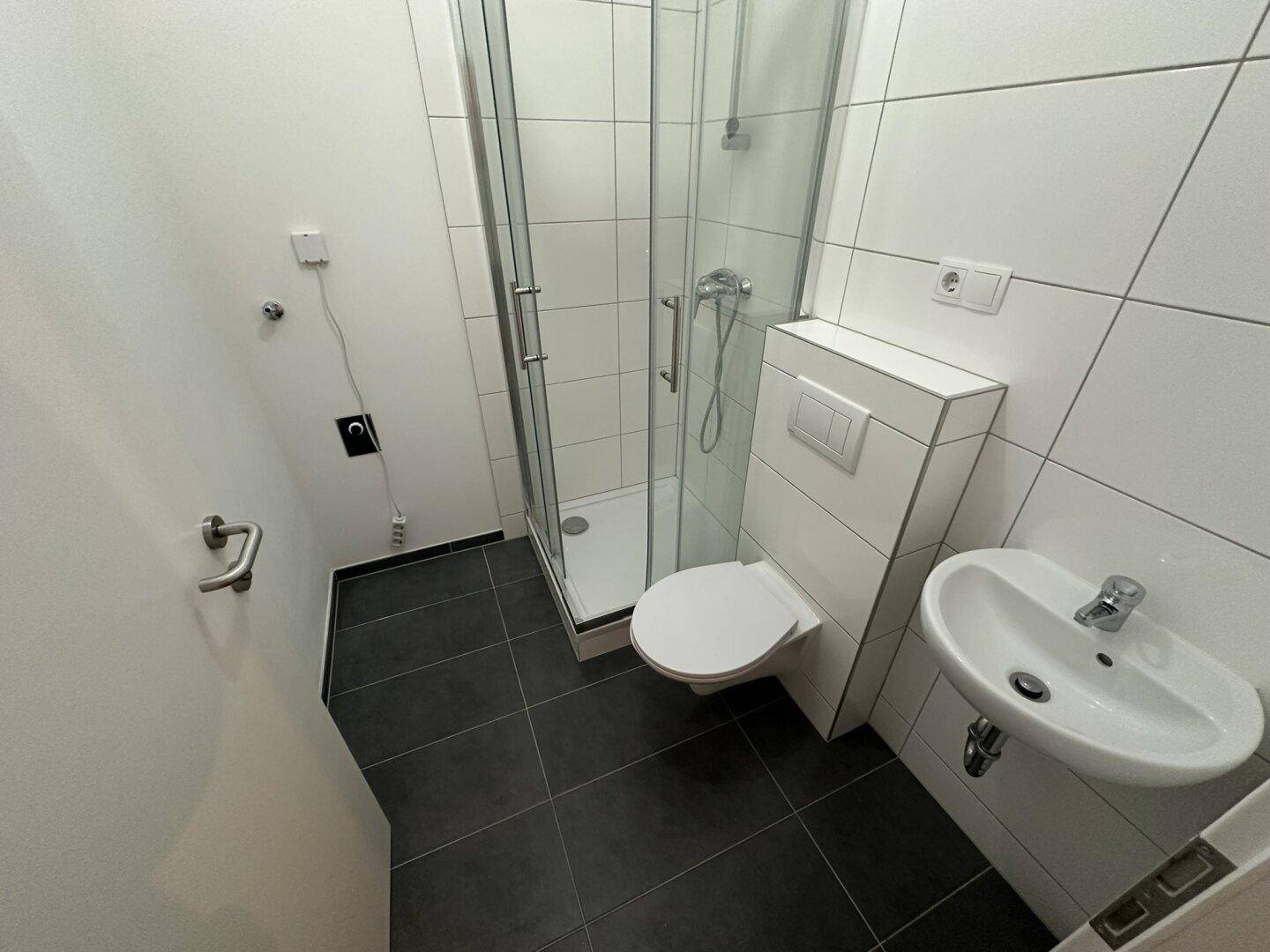 Modernes Badezimmer mit Duschkabine, wandhängendem WC und kleinem Waschbecken.