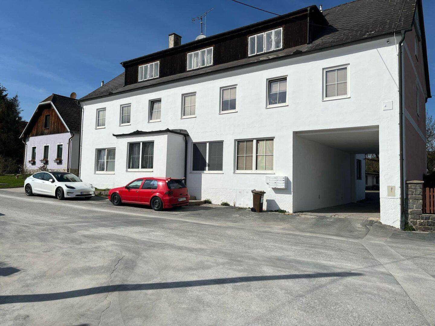 Weißes Mehrfamilienhaus mit mehreren Fenstern und einem überdachten Eingangsbereich.