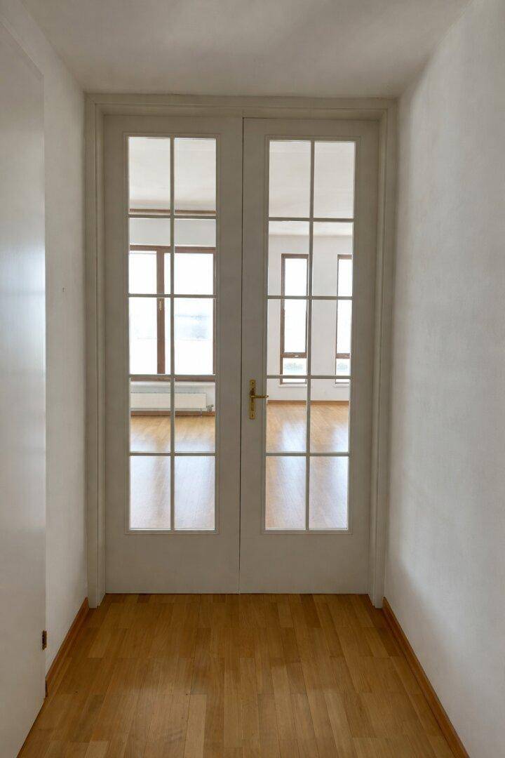 Heller Flur mit Parkettboden und Glastüren, die zu einem weiteren Raum führen.