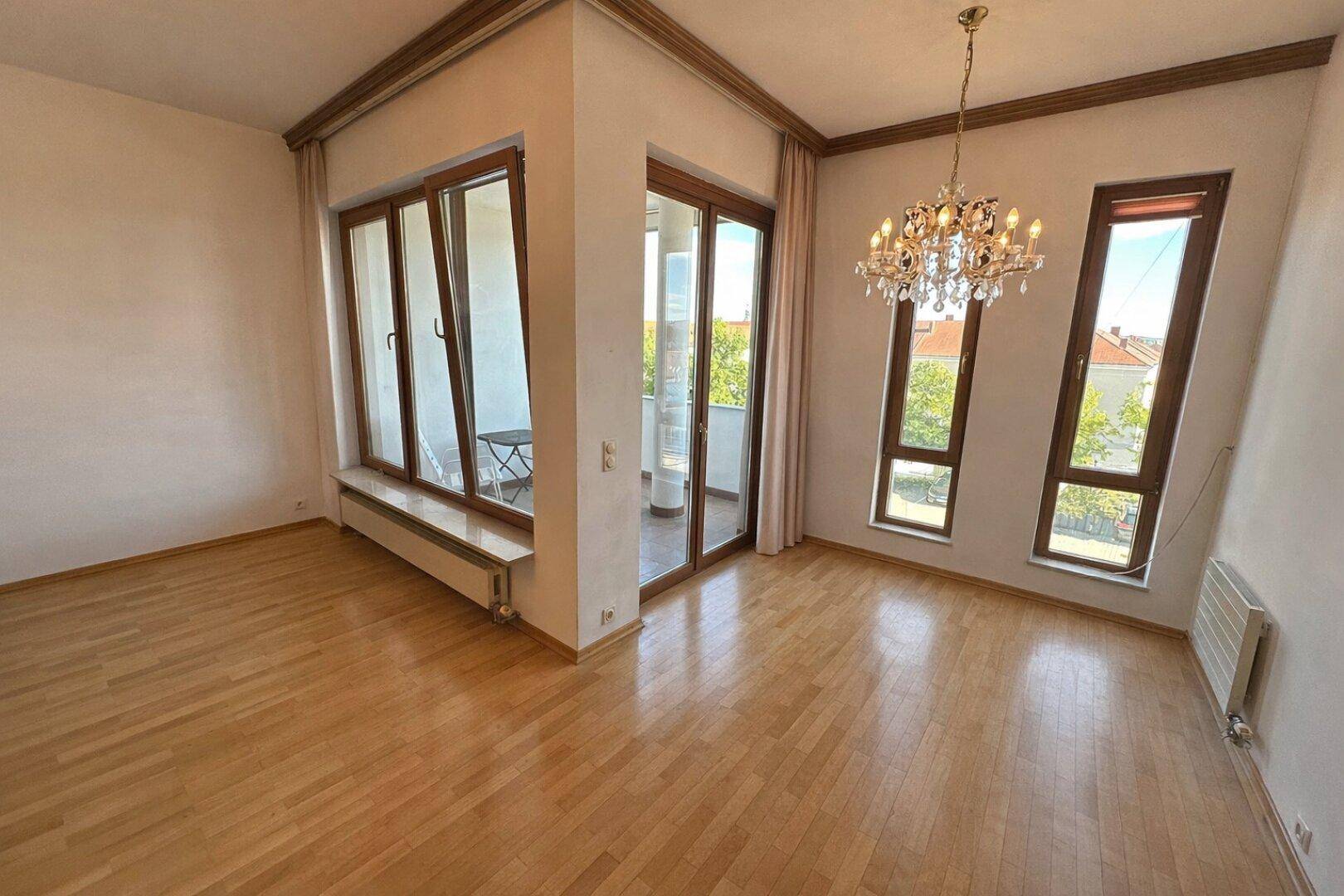 Helles Wohnzimmer mit Parkettboden, großen Fenstern und Zugang zu einem Balkon.