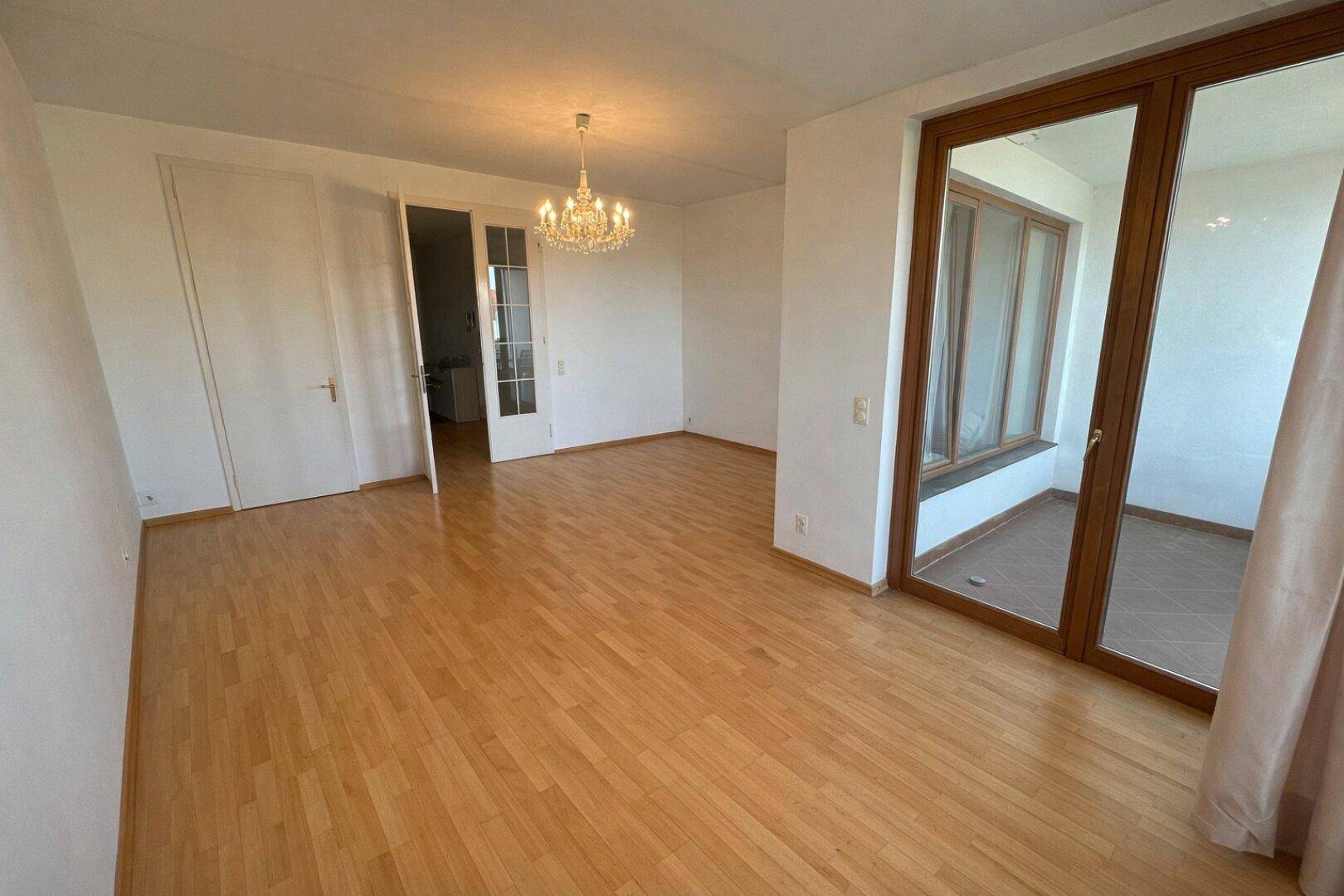 Geräumiges Wohnzimmer mit Parkettboden und Blick auf den angrenzenden Küchenbereich.