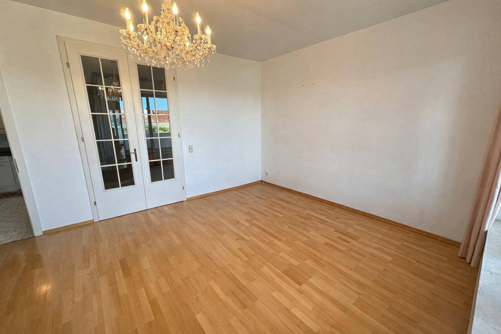 Heller Wohnbereich mit Parkettboden und einer eleganten Kristall-Deckenleuchte.