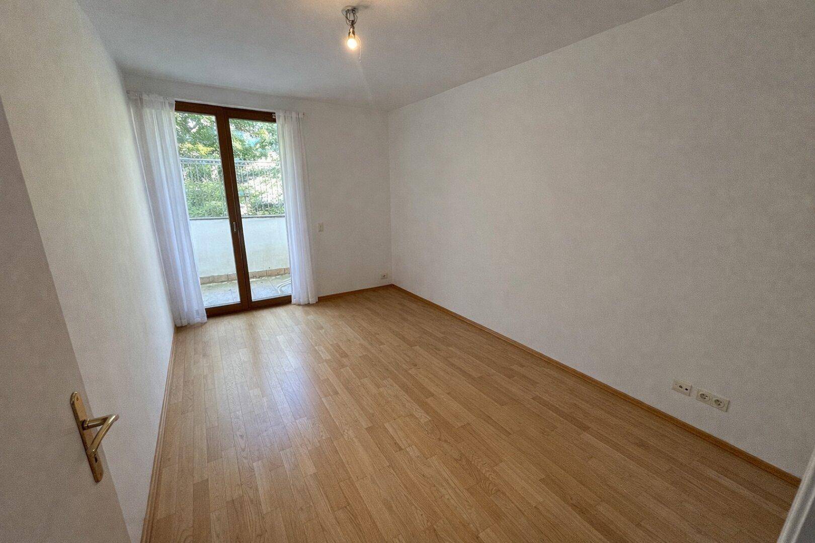 Helles Zimmer mit Parkettboden und direktem Zugang zu einem kleinen Balkon.
