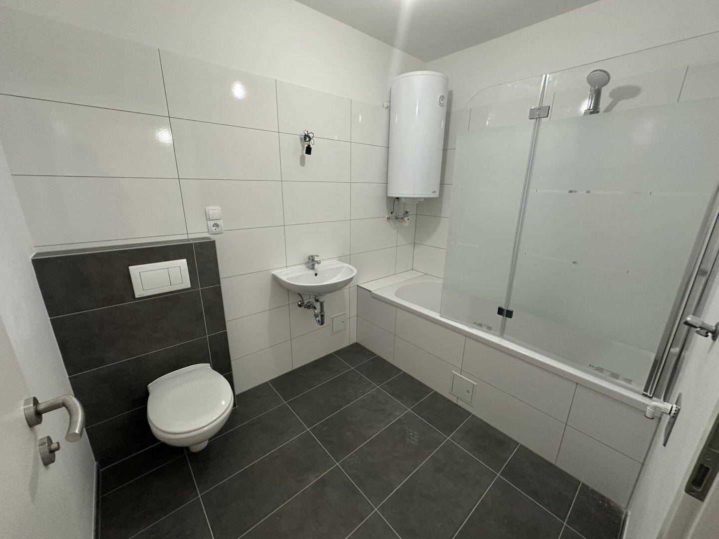 Modernes Badezimmer mit Badewanne, Duschabtrennung, WC und dunklen Bodenfliesen.