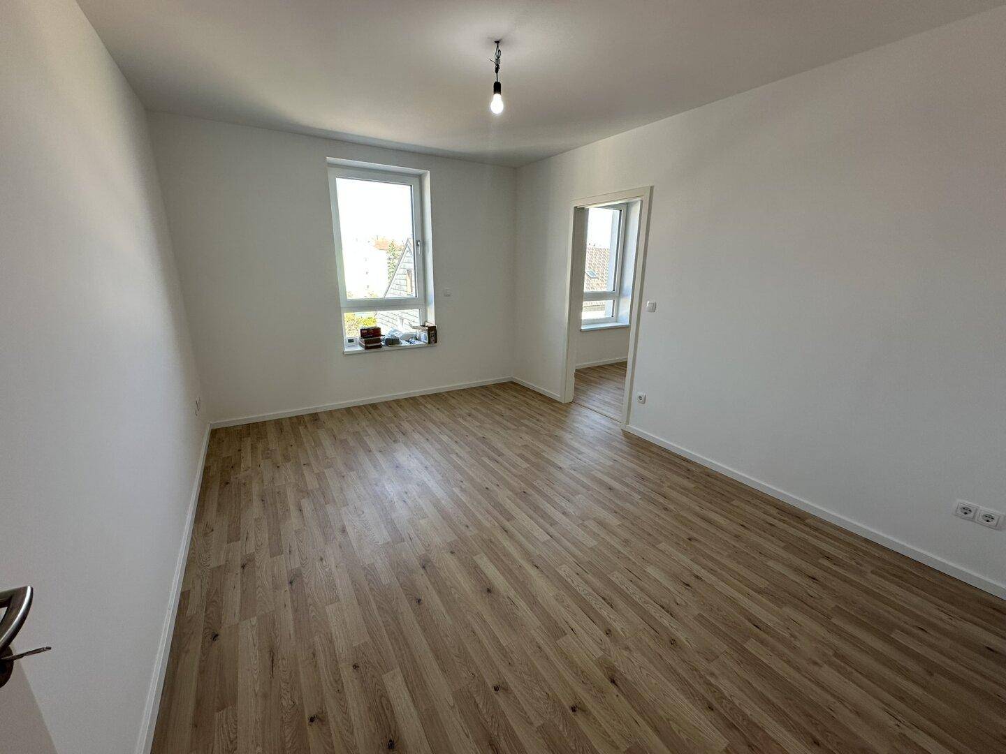 Heller, leerer Raum mit Holzfußboden und großen Fenstern, ideal als Wohn- oder Schlafzimmer.