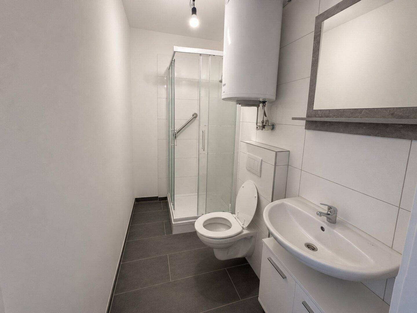 Modernes Badezimmer mit Dusche, WC, Waschbecken und einem Warmwasserboiler an der Wand.