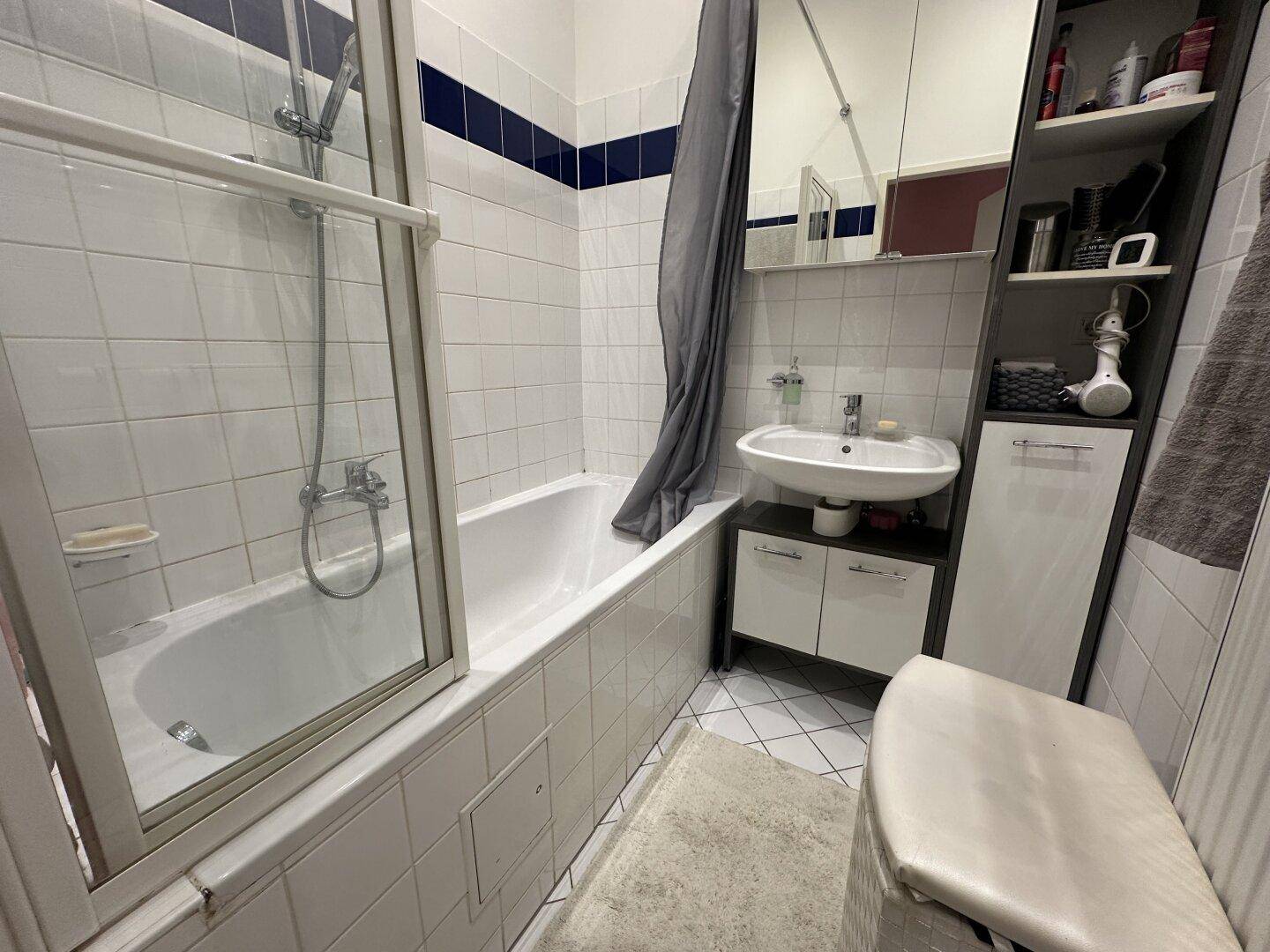Helles Badezimmer mit Badewanne, Duschabtrennung und weißen Fliesen.