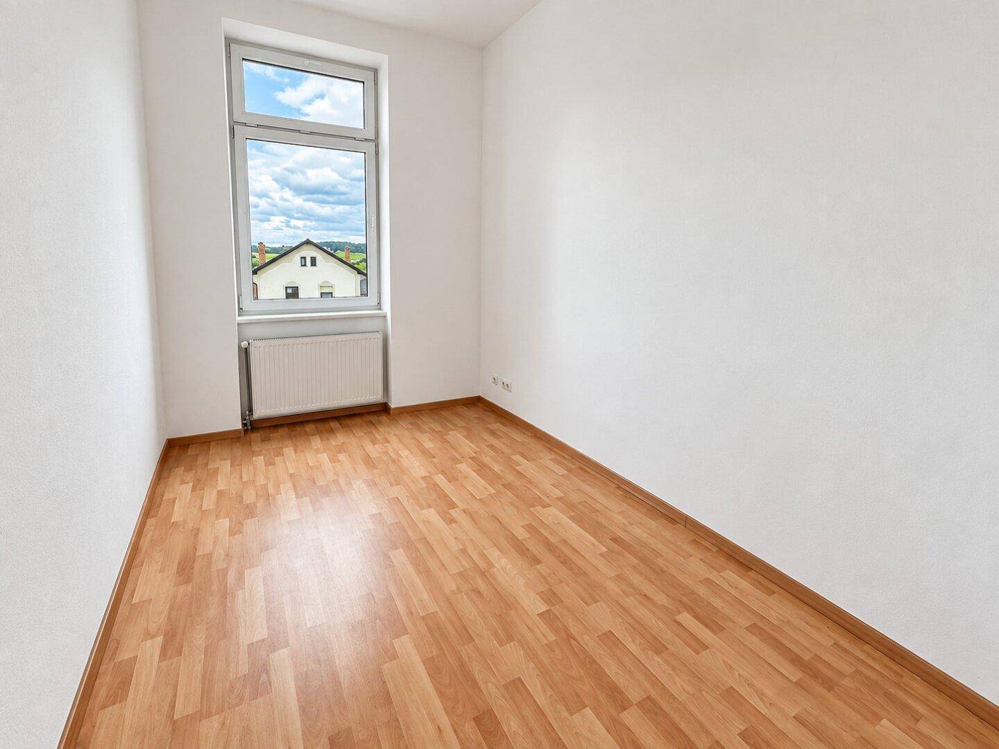 Helles Schlafzimmer mit Laminatboden, weißen Wänden und einem Fenster mit Ausblick.