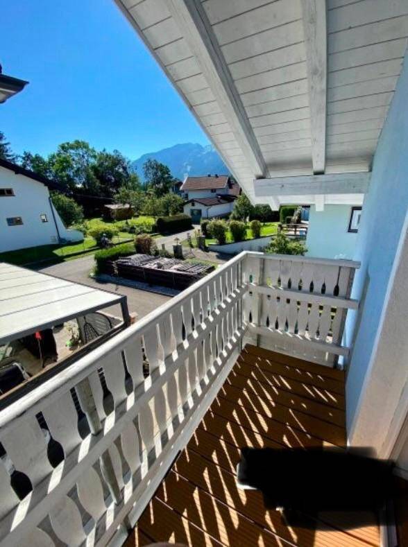 Holzbalkon mit weißem Geländer und weitem Blick auf die Berge und Umgebung.