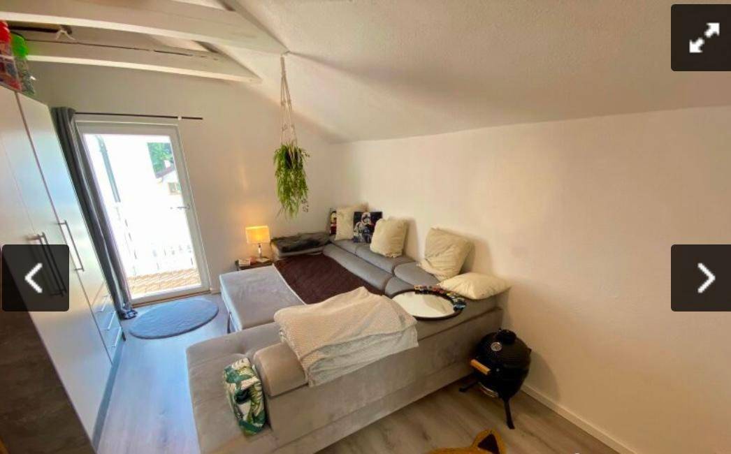 Gemütliches Wohnzimmer im Dachgeschoss mit großem Ecksofa und Zugang zum Balkon.