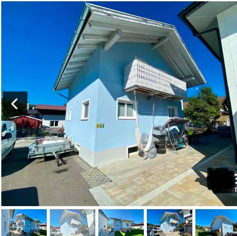 Seitenansicht des blauen Hauses mit Balkon und gepflasterter Fläche an einem sonnigen Tag.