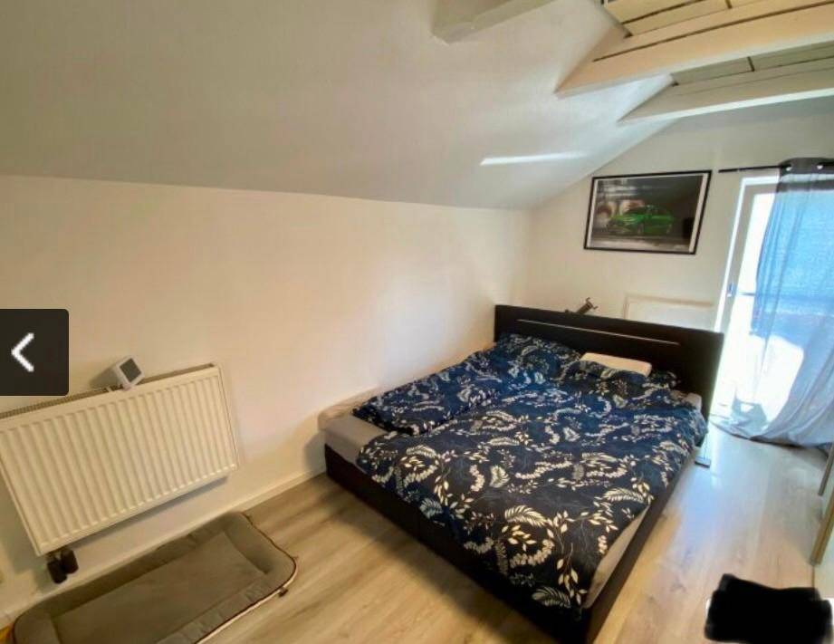 Schlafzimmer im Dachgeschoss mit Doppelbett, Heizkörper und Zugang zum Balkon.