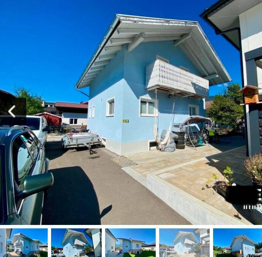 Seitenansicht des blauen Hauses mit Balkon und gepflasterter Fläche unter blauem Himmel.