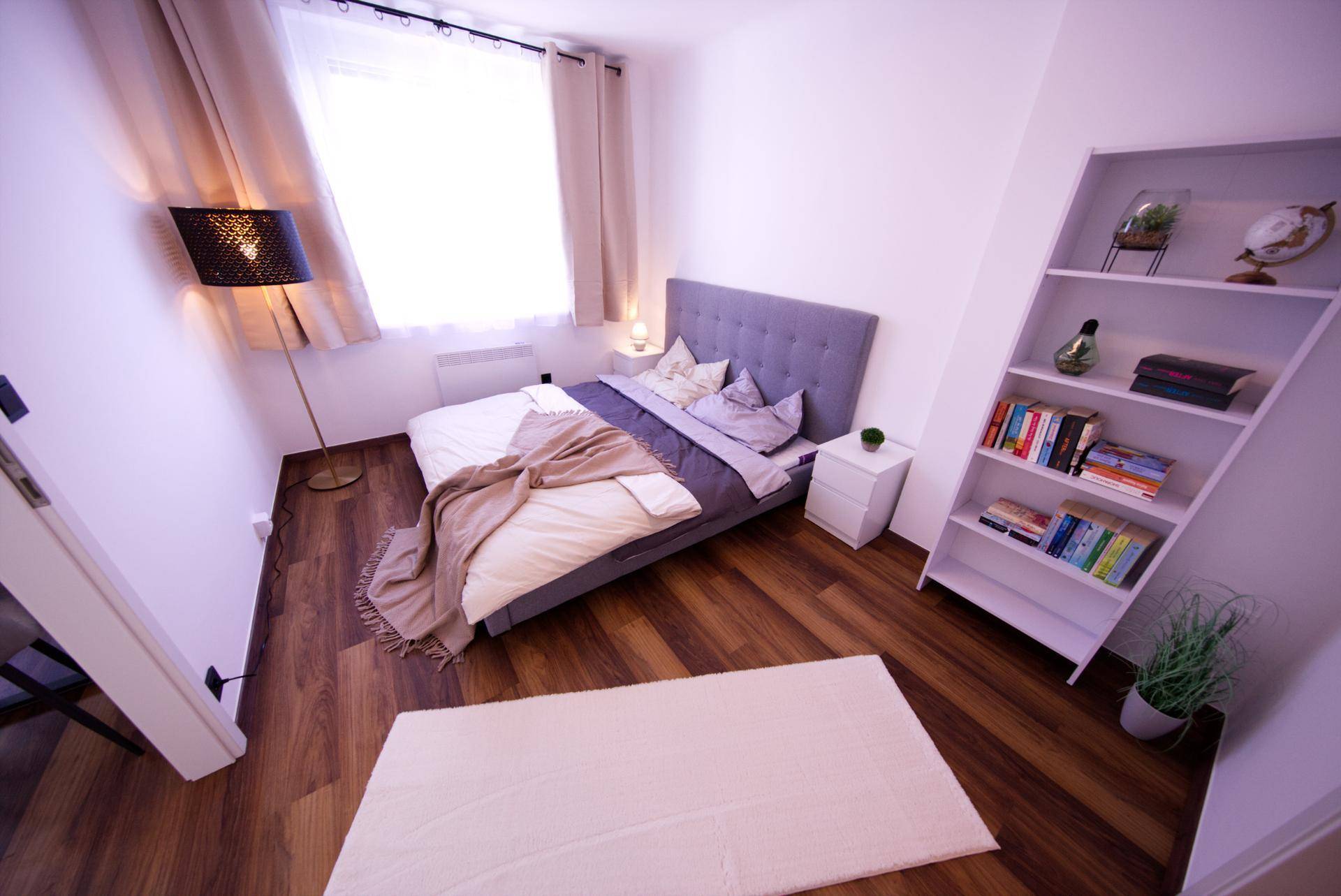 Schlafzimmer mit Doppelbett, Bücherregal und Holzboden, hell und modern eingerichtet.